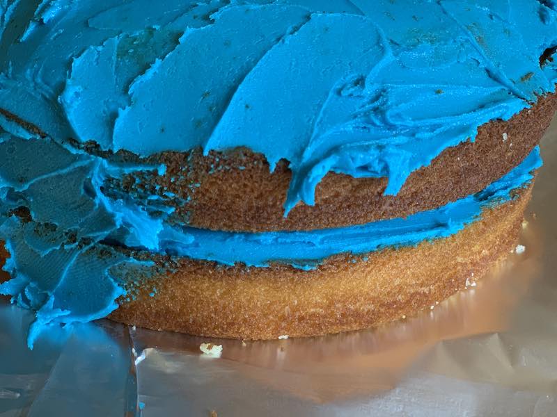 The layered cake getting decorated with blue icing